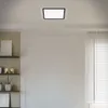 A rectangular LED panel light is mounted on a white ceiling above a wall with decorative molding and a window with blinds. Produktbild-Vorschau