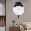 A cat-shaped wall clock with a pendulum is displayed on a wall above a wooden nightstand with flowers and a vase. Produktbild-Vorschau