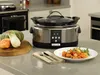 A Crockpot slow cooker is shown on a kitchen counter next to fresh vegetables and a plate of food. Produktbild-Vorschau