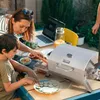 A mother and son are preparing food outdoors, with a portable grill on a table. Produktbild-Vorschau