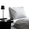 A close-up view of a bed with striped bedding and a bedside table with a lamp and a mug. Produktbild-Vorschau
