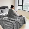 A woman sits on a bed, wrapped in a gray blanket, looking out a window. Produktbild-Vorschau