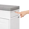 A close-up shot of a person's finger pressing on a drawer of a white shoe cabinet with a gray upholstered seat. Produktbild-Vorschau