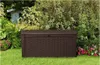 A brown storage box sits on a green lawn in front of lush green bushes and some pink flowers. Produktbild-Vorschau