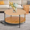 A round, two-tiered coffee table with a wood-grain finish is placed on a gray carpet in front of a sofa. A decorative bear figurine holding a bouquet of yellow tulips sits on the top tier of the table. Produktbild-Vorschau