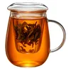 A glass tea mug filled with amber-colored tea and loose tea leaves in an infuser. Produktbild-Vorschau