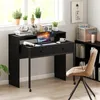 A black desk with a laptop, books, and plants is set up in a room with a window and a bookshelf. Náhled obrázku produktu
