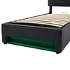 A close-up view of the lower portion of a black upholstered bed frame with wooden slats visible and green LED lighting underneath. Náhľad obrázku produktu