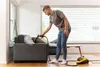 A man is using a steam cleaner on a sofa in a living room. Náhled obrázku produktu