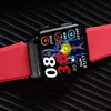 A smartwatch with a red strap is displayed on a black ribbed surface. Náhled obrázku produktu
