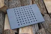 A square metal grate with many holes is placed on top of a pile of chopped wood. Produktbild-Vorschau