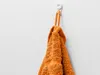 An orange towel hanging on a white hook against a white wall. Anteprima dell’immagine prodotto
