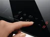 A person's finger is pressing a button on a black induction cooktop. Voir les images du produit