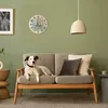 A dog is lying on a sofa in a living room, with a clock on the wall. Produktbild-Vorschau