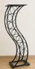 A black metal wine rack with a curved, wave-like design, standing on a wooden floor against a light-colored wall. Anteprima dell’immagine prodotto