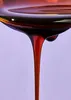 A close-up shot of dark brown syrup being poured from a spoon. Produktbild-Vorschau