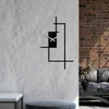 A modern black metal wall clock with a minimalist design is mounted on a textured white wall, with a brick wall and a sofa visible in the background. Anteprima dell’immagine prodotto