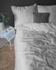 A neatly made bed with striped bedding and a grey cushion, next to a small side table with a book and a plant. Anteprima dell’immagine prodotto