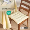 A chair with a cream-colored seat cushion is placed next to a table covered with a cream-colored tablecloth. A bowl and plates are on the table. Anteprima dell’immagine prodotto