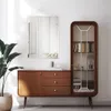 A modern wooden cabinet with drawers and a glass-doored display cabinet, a mirror on the wall above it, and a large potted plant to the left. Produktbild-Vorschau