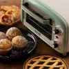 A vintage-style mini oven is shown on a wooden table, surrounded by baked goods like muffins, mini pizzas, and a tart. Anteprima dell’immagine prodotto