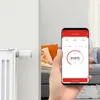A hand holding a smartphone displaying a smart heating app, with a radiator and thermostat in the background. Náhľad obrázku produktu