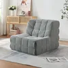 A grey upholstered floor chair is placed on a rug in a living room setting, with a wooden console table and artwork in the background.