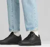 A close-up shot of a person wearing black Puma sneakers and light blue jeans. Voir les images du produit
