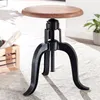 A close-up shot of an adjustable height stool with a wooden seat and black metal base, placed on a textured rug. Produktbild-Vorschau