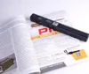 A black handheld scanner is placed on an open magazine, with the scanner partially covering the magazine's content. Produktbild-Vorschau