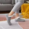 Graue Zopfstrick-Hausschuhe-Socken mit weißem Kunstfell-Innenfutter, getragen von einer Person, die auf einem gemusterten Teppich steht Náhľad obrázku produktu