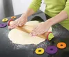 A person is using a rolling pin to flatten dough on a black surface. Several colorful rings are scattered around the dough. Produktbild-Vorschau