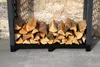 A metal firewood rack filled with logs, placed against a stone wall. Produktbild-Vorschau