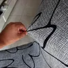 A hand is stretching a grey fabric with a black pattern, likely a chair cover. Produktbild-Vorschau
