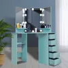 A light blue vanity table with a tri-fold mirror and LED lights, set against a blue wall with a potted plant to the left and a white curtain to the right. Voir les images du produit