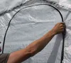 A person's arm and hand are shown zipping up a white tent or greenhouse. Voir les images du produit