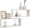 Two white cube shelves are displayed against a white background. The top shelf holds two decorative vases and a diffuser. The bottom shelf displays a starfish decoration and a small vase with reeds. To the left of the bottom shelf are two framed pictures. Náhľad obrázku produktu