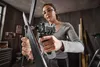 A woman is using a cordless impact driver to work on a metal object in a workshop. Produktbild-Vorschau