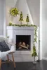 A festive Christmas display featuring a decorated fireplace with a garland, small Christmas trees, and a wreath. Produktbild-Vorschau