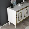 A close-up view of a white sideboard with gold accents, placed against a dark gray wall and on a light wooden floor. Produktbild-Vorschau