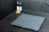 A grey shower mat is placed on a tiled floor in a shower stall, next to two bottles of toiletries and a sponge. Produktbild-Vorschau