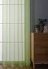 A green sheer curtain hangs in front of a window, with a wooden dresser and a potted plant to the right. Produktbild-Vorschau
