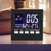 A digital alarm clock displaying time, weather icons, temperature, and humidity, placed on a surface with a blurred background. Produktbild-Vorschau
