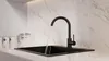 A black kitchen faucet with water running into a black sink, set against a marble-patterned backsplash. Produktbild-Vorschau