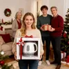 A family is gathered around a Christmas tree, with a young woman in the foreground holding a gift-wrapped electric kettle. Produktbild-Vorschau