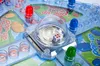 A close-up view of a board game with colorful pieces and a dice in a clear dome. Náhľad obrázku produktu