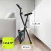 A black and blue exercise bike is shown in a room next to a sofa and a white cabinet. Dimensions are indicated with text overlays. Anteprima dell’immagine prodotto