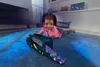 A young girl is playing with a toy truck and car on a blue carpet in a room. Anteprima dell’immagine prodotto