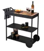 A black outdoor kitchen serving cart with wooden accents, holding wine glasses, a bottle of wine, fruit, and jars. Produktbild-Vorschau