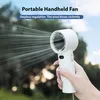 A hand holding a white portable fan outdoors, with trees and sky in the background. Náhled obrázku produktu